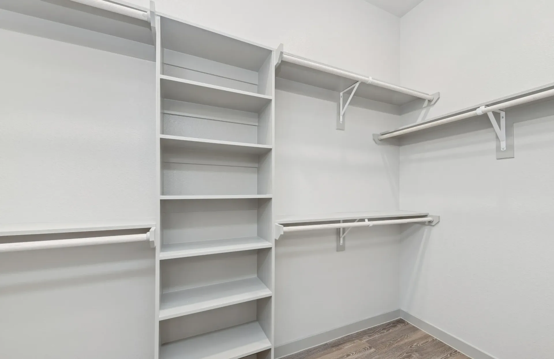 Walk-in closet with white built-in shelves and multiple hanging rods.