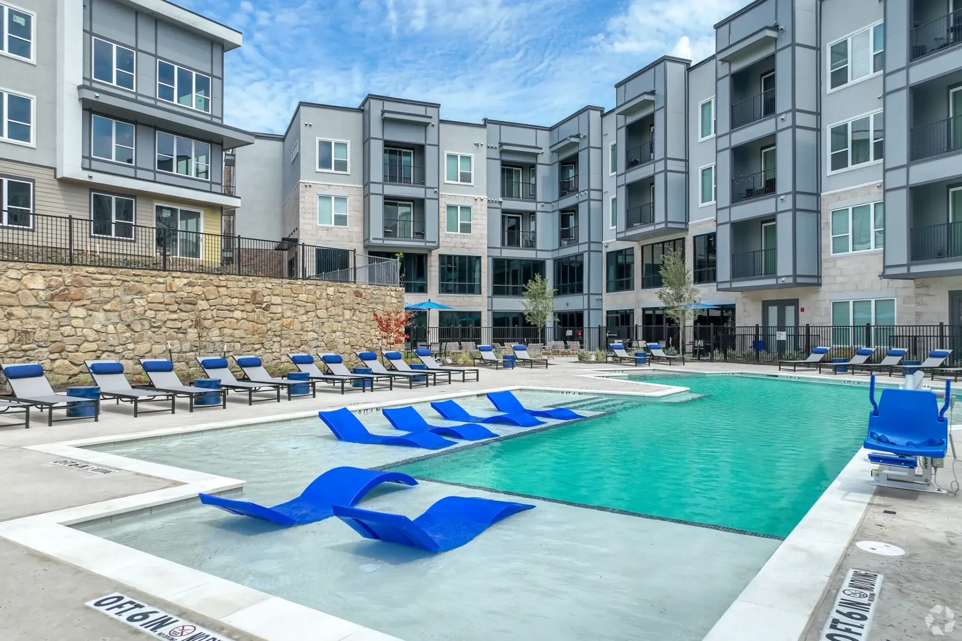 Outdoor pool area at a modern apartment complex with blue lounge chairs.