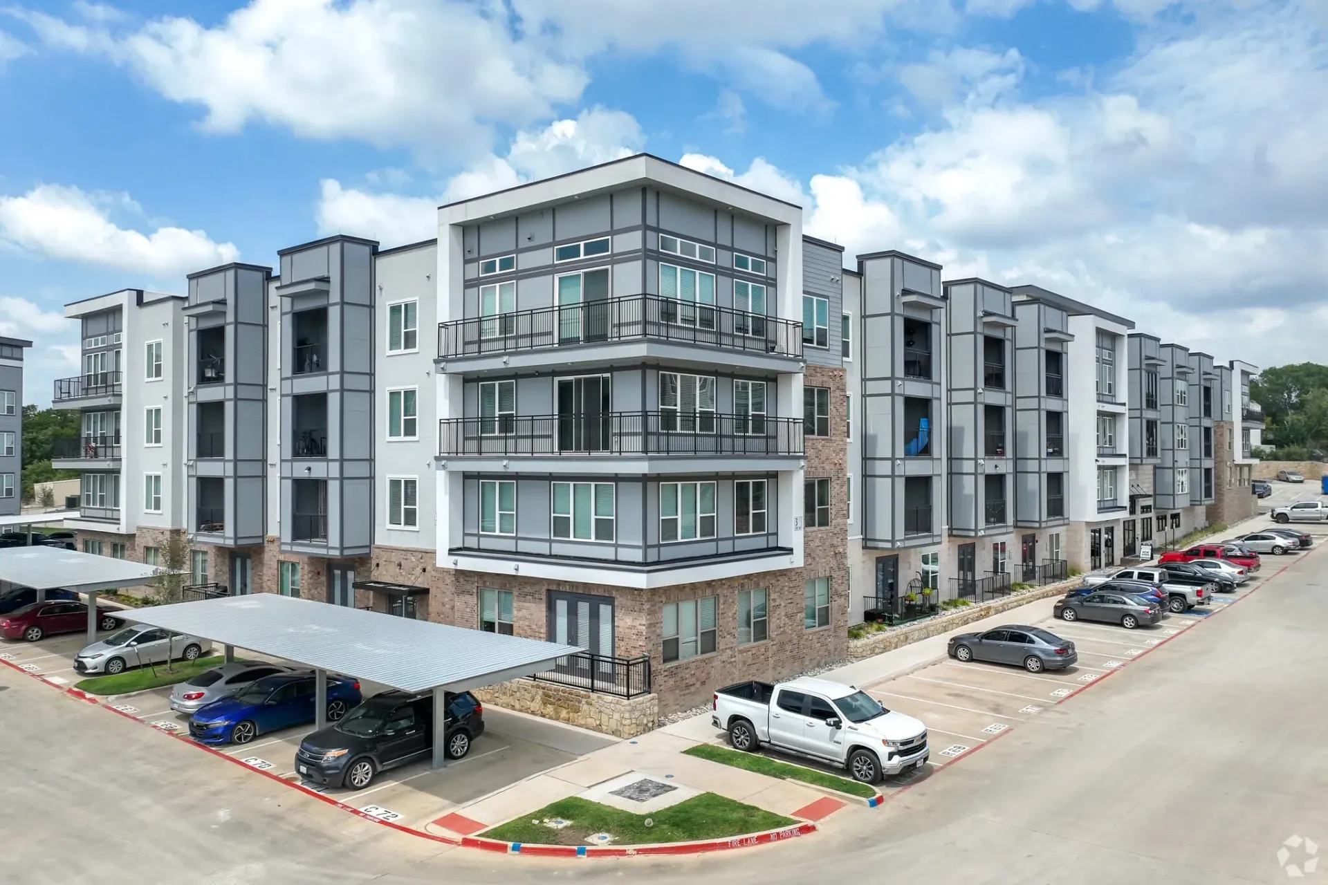 Exterior view of a modern apartment building complex with balconies and a parking lot.