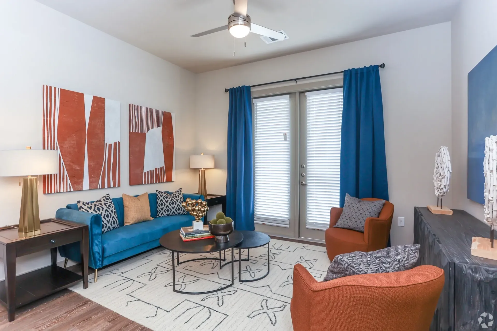 Living room in an apartment with a blue sofa, orange chairs, and abstract wall art.