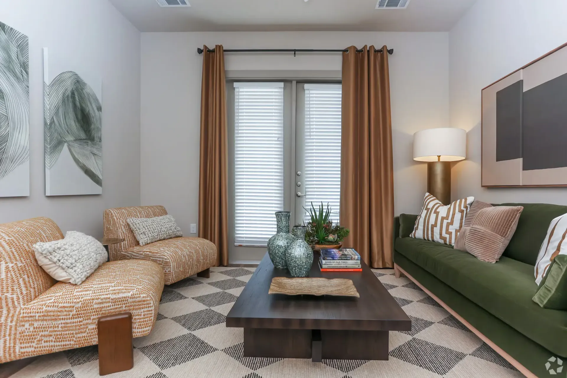Living room in an apartment featuring a green sofa, two orange patterned chairs, a dark wood coffee table, and brown drapes.