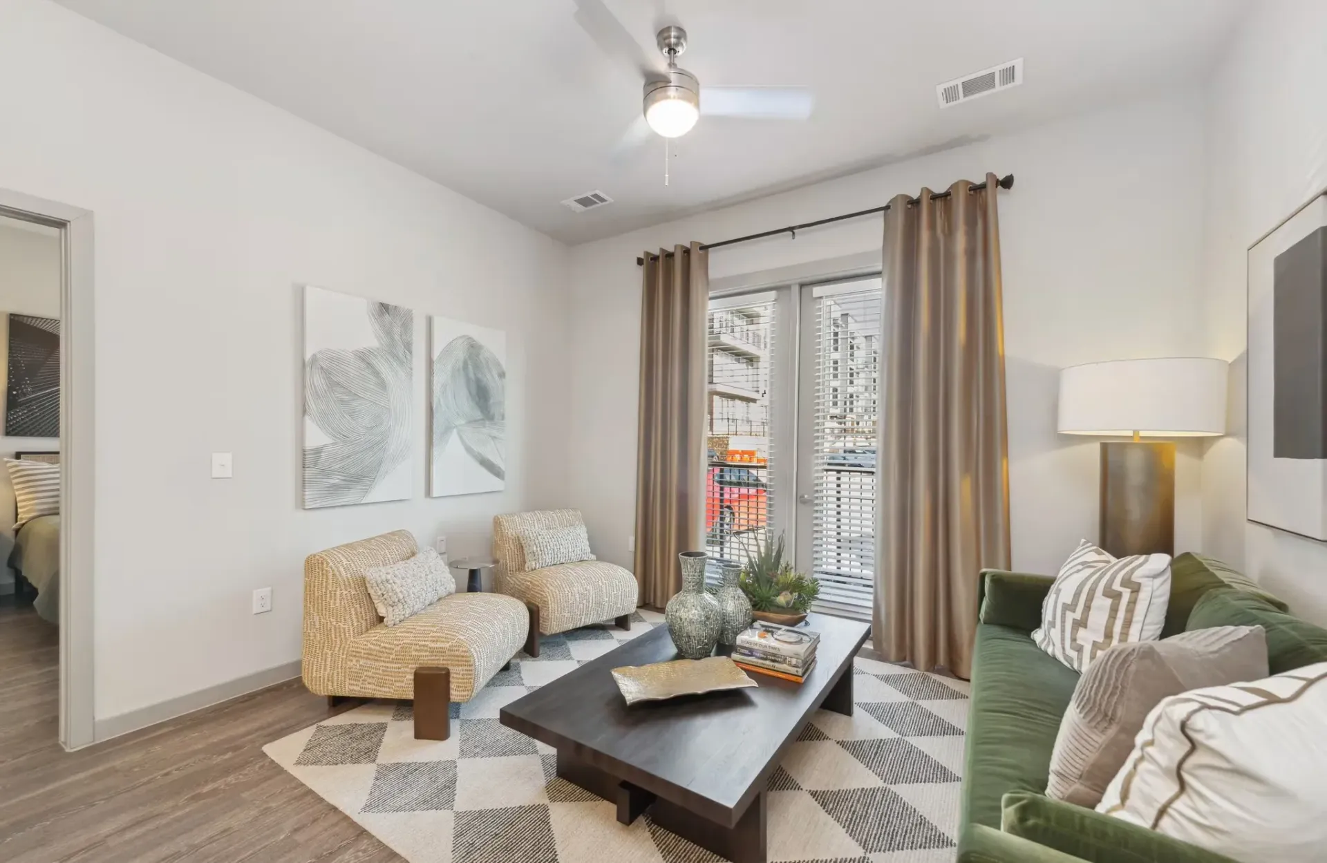 Living room in a modern apartment with a green sofa, beige chairs, and balcony doors.