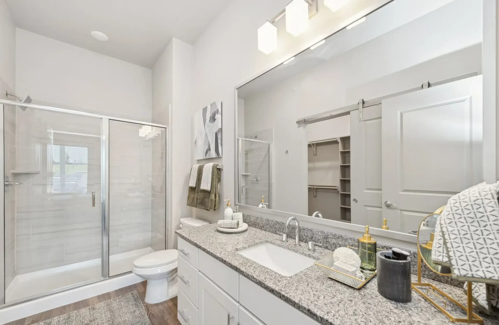 Modern apartment bathroom with granite vanity, large mirror, and glass-enclosed shower.