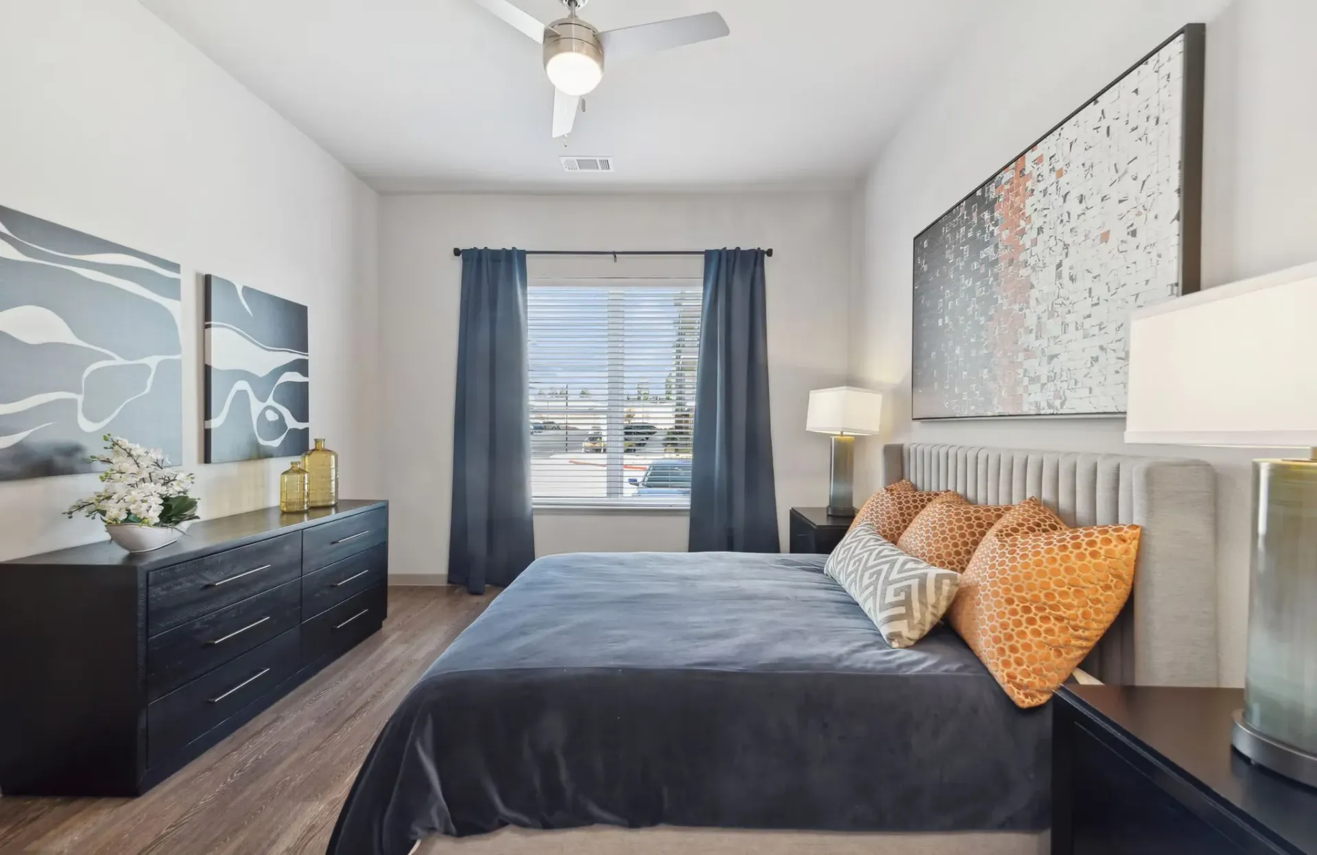 Bedroom with blue bed, gray walls, two windows, and black nightstand  at  Ennova Fulshear in Fulshear, TX.