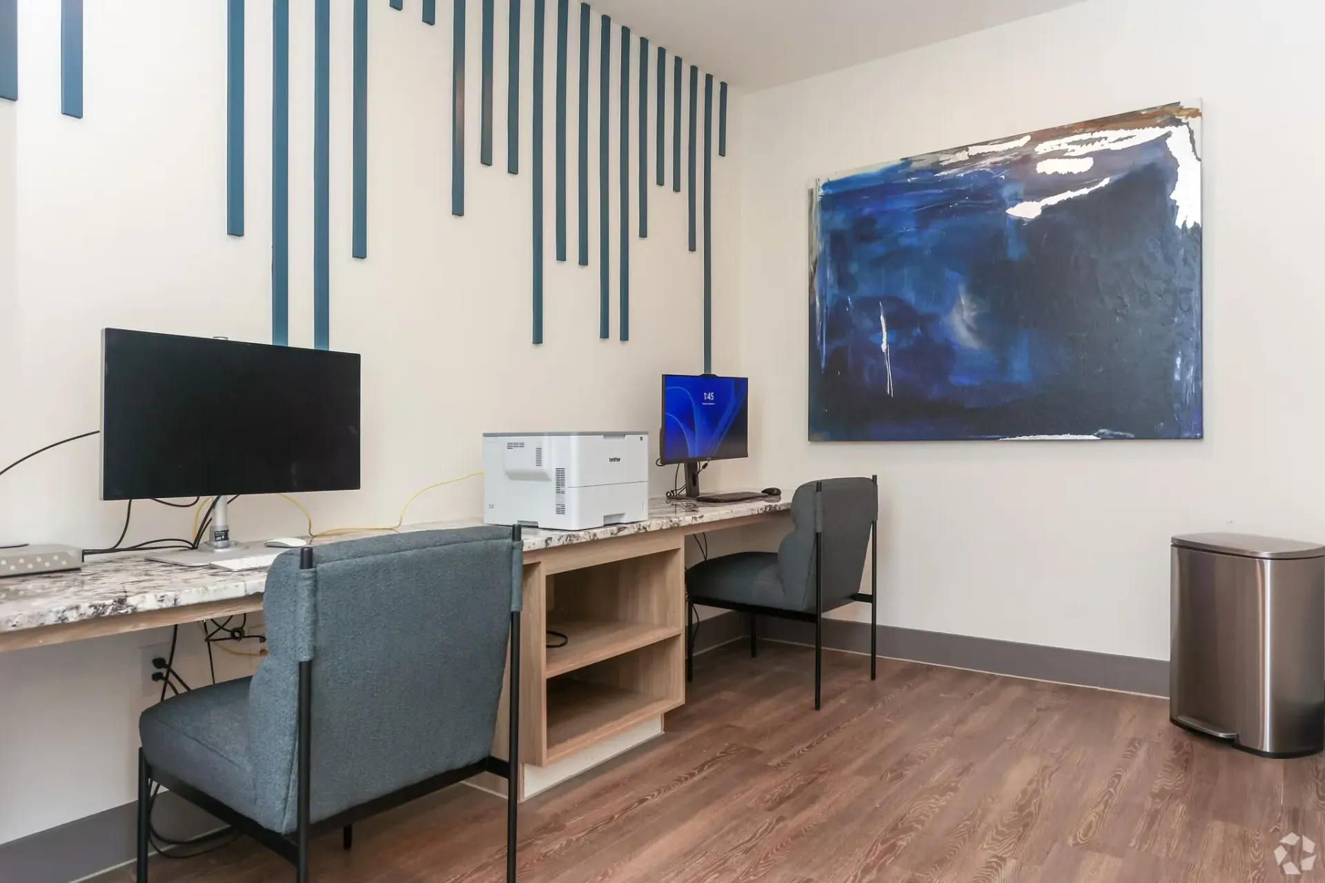 Community computer room with two desks, monitors, printer, and abstract wall art.