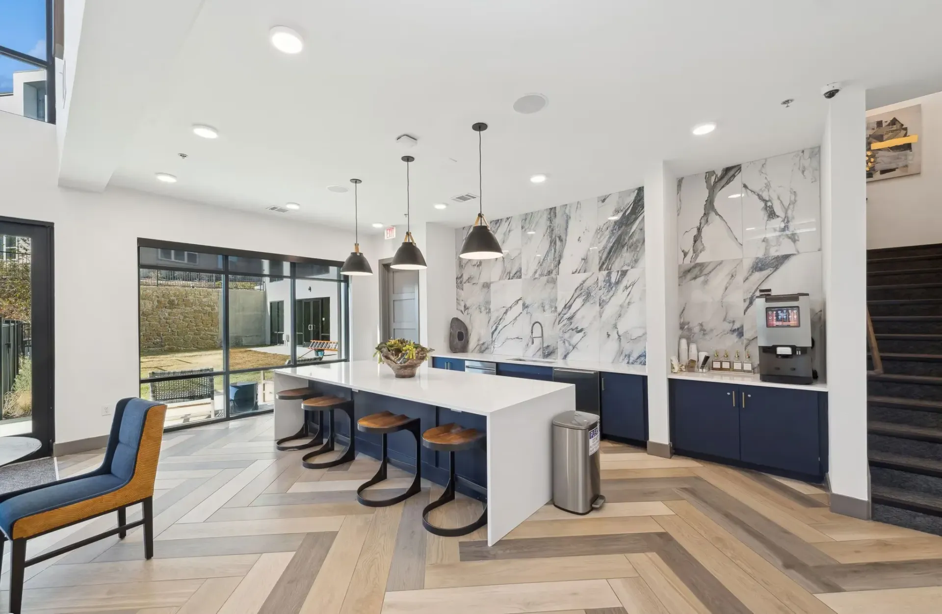 Modern community kitchen and lounge with marble backsplash, island, and pendant lights.