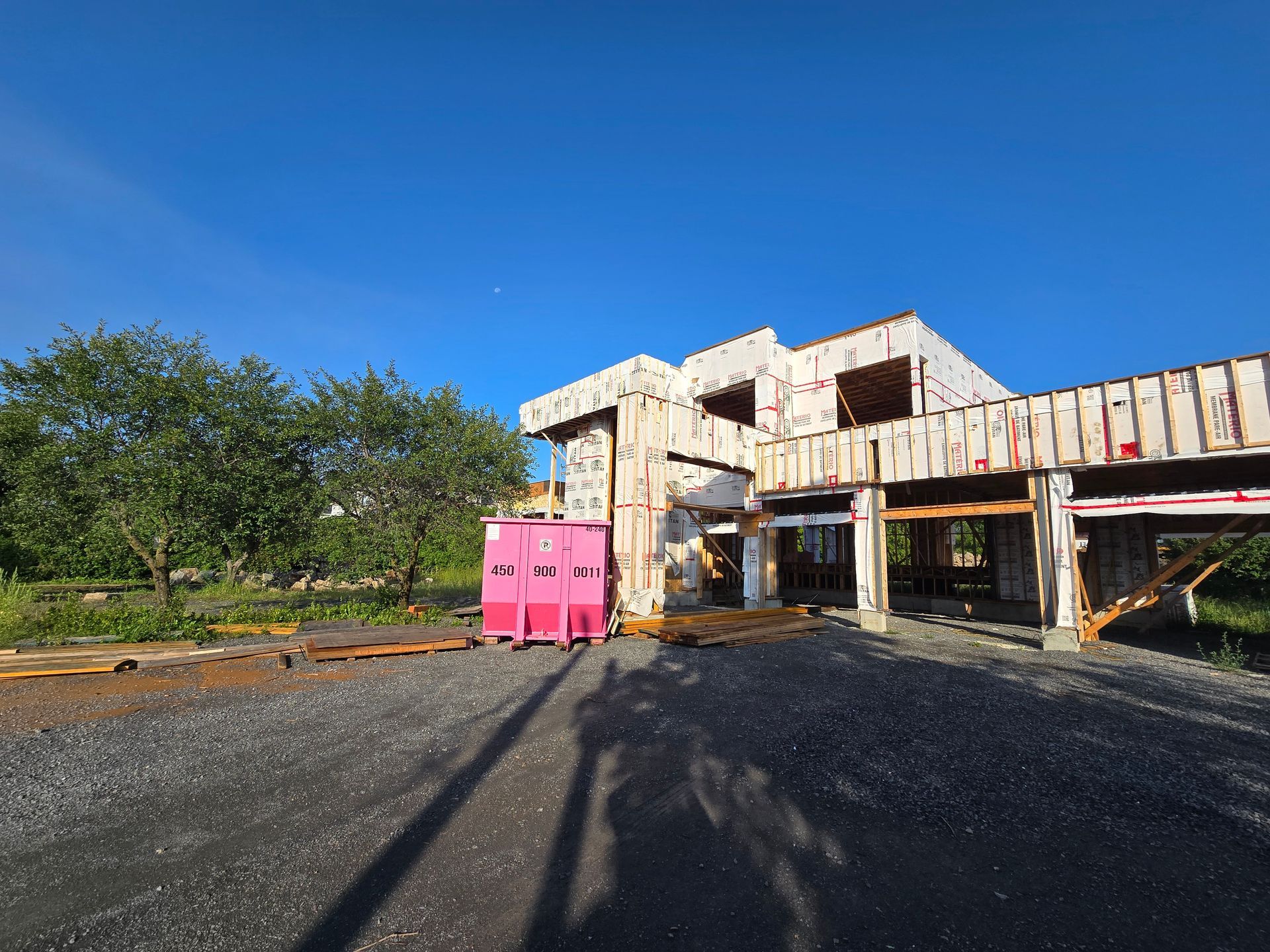 A large building under construction with a pink dumpster in front of it.