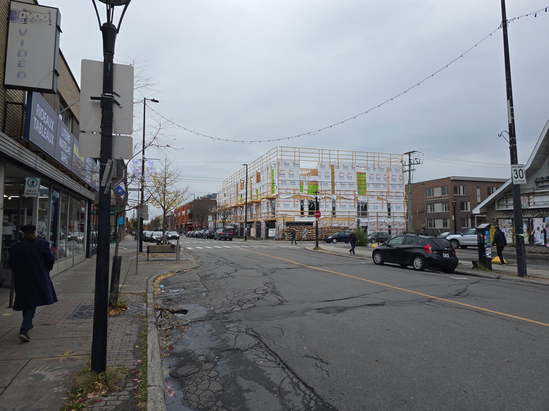 A street with cars parked on the side of it and a building under construction in the background.
