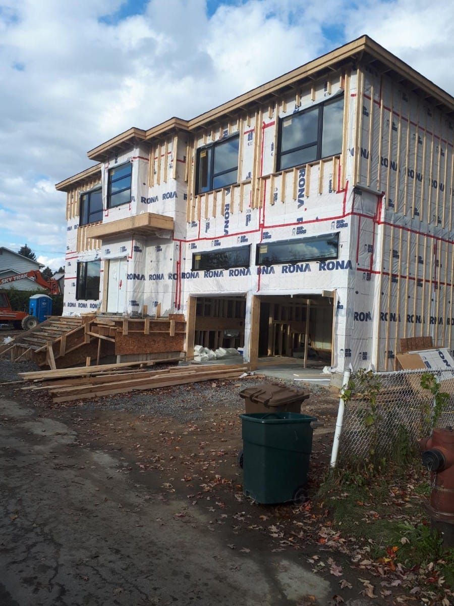 Une grande maison en construction avec une poubelle verte devant
