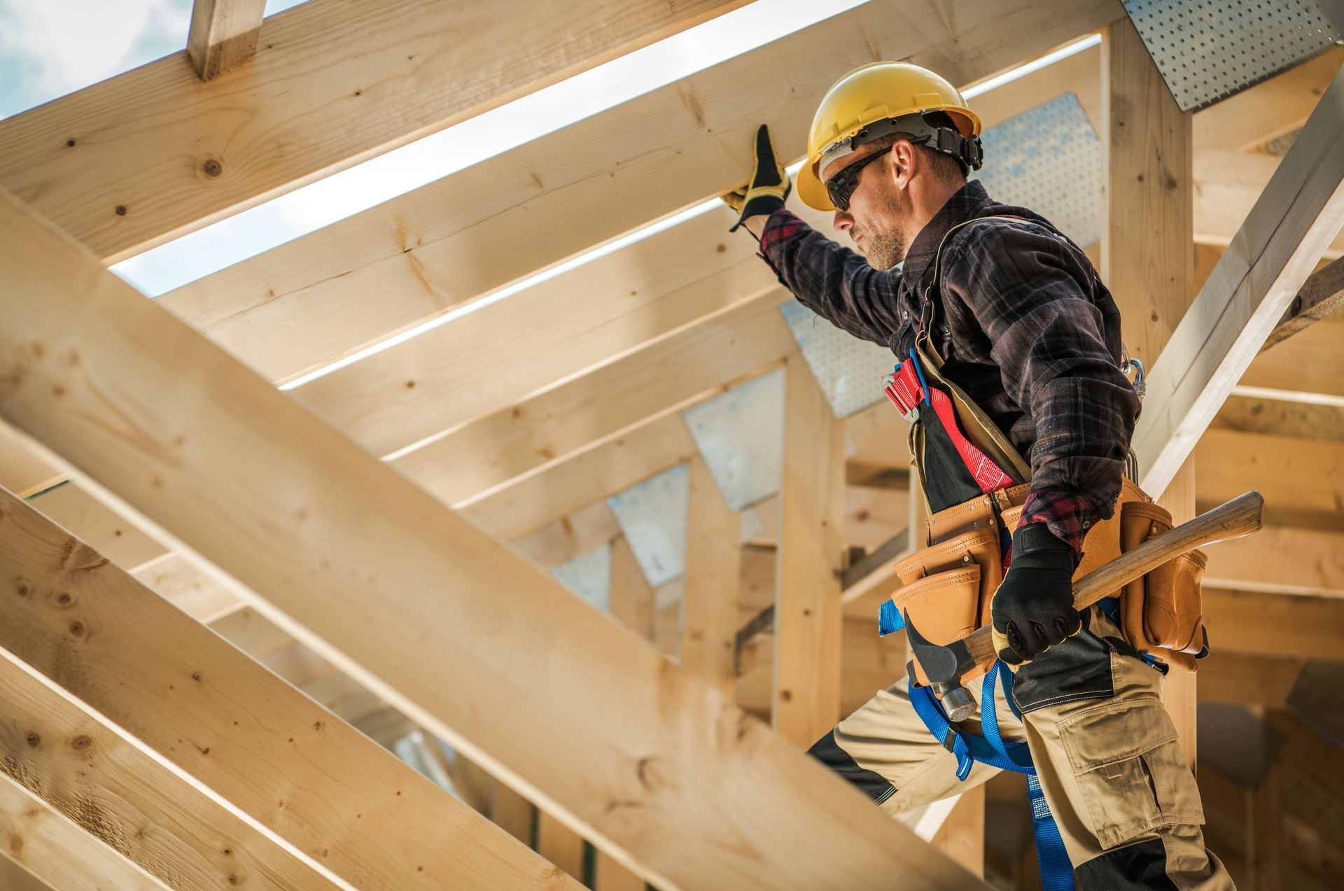 Un ouvrier du bâtiment, casqué de jaune, inspecte la structure sur des poutres en bois.