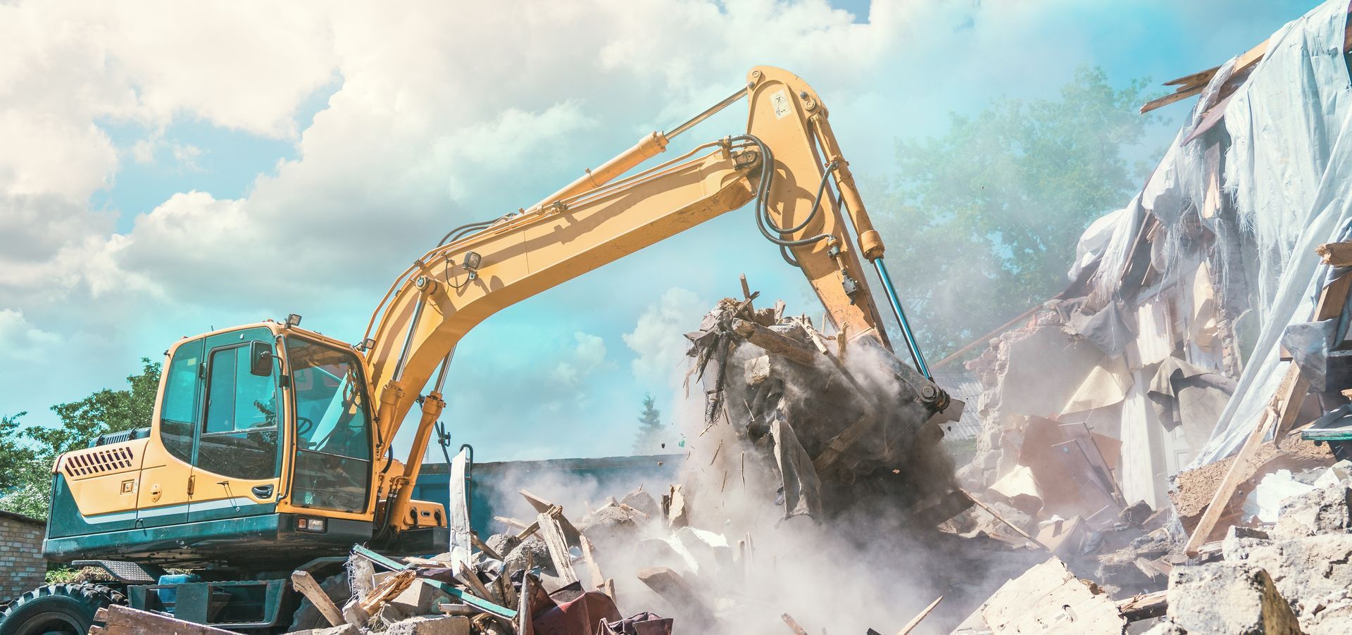 Yellow excavator demolishing a rocky cliff, kicking up dust and debris
