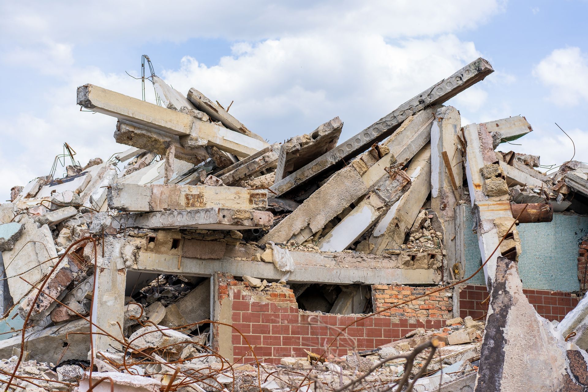 Collapsed brick building with broken concrete beams and rubble under a cloudy sky