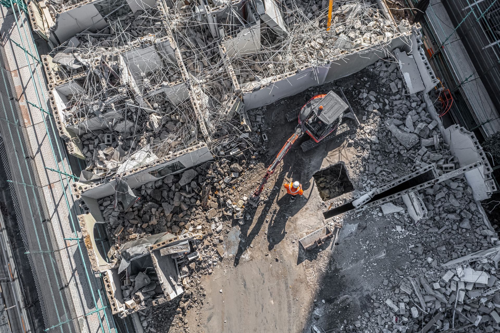 Aerial view of a demolition site with heavy machinery amid rubble and broken concrete.