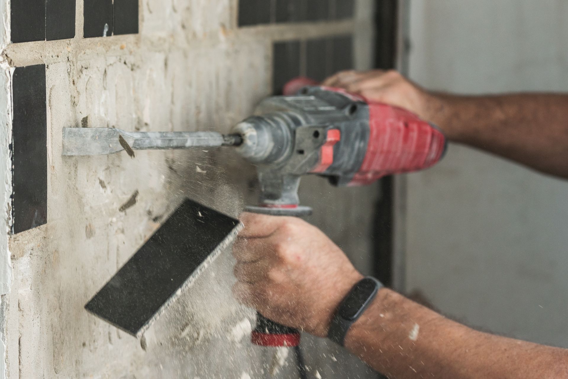 Person using a red power drill to bore into a concrete wall indoors