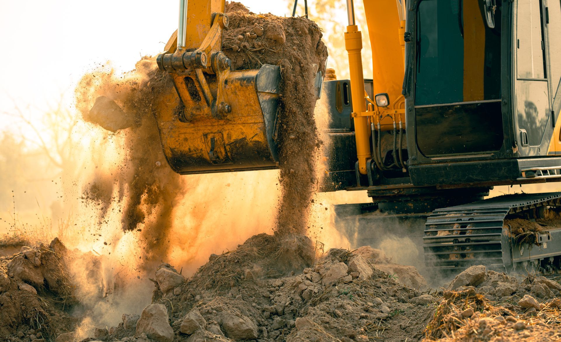 Excavator dumping dirt at a construction site, raising a cloud of dust