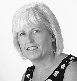 Portrait of a smiling woman with short light hair in a patterned sleeveless top, against a plain background
