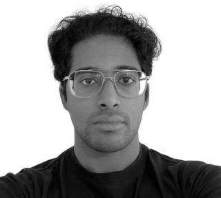 Portrait of a person wearing glasses and a dark shirt, looking at the camera against a light background