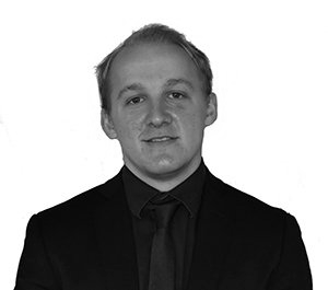 Black-and-white portrait of a man in a dark suit and tie against a plain background