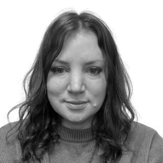 Black-and-white headshot of a person with shoulder-length hair wearing a sweater, looking at the camera.