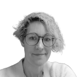 Portrait of a person with glasses and curly hair, wearing a light sweater, smiling softly on a plain background