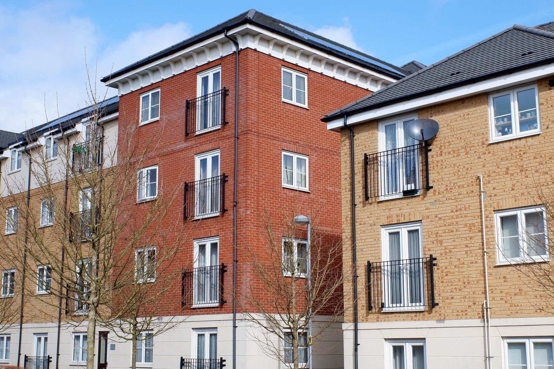 Red-brick and beige apartment buildings with windows and trees under a blue sky