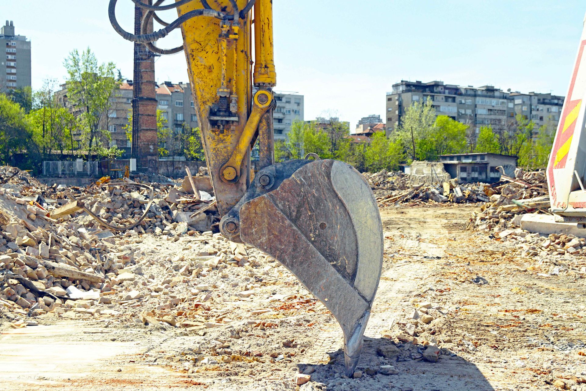 Excavator bucket resting on rubble at active demolition site with urban background. Excavator bucket resting on rubble at active demolition site with urban background.