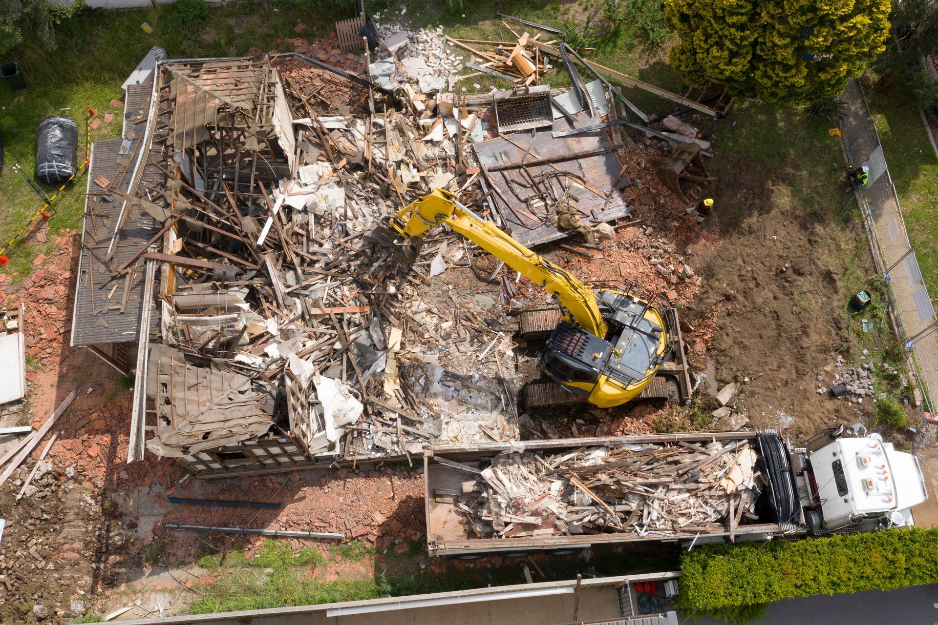 Aerial view of a yellow excavator and truck at a site managed by a demolition contractor.