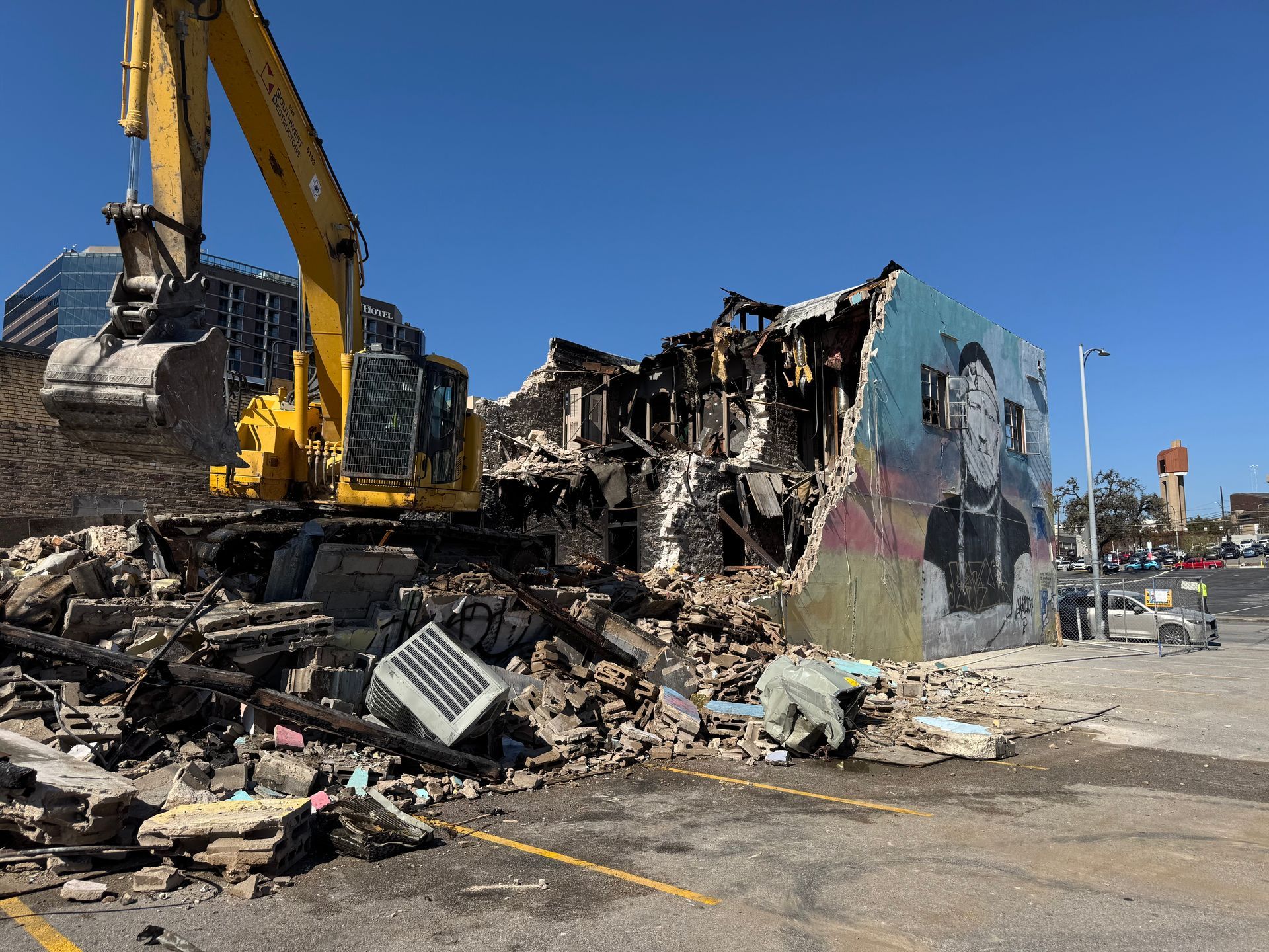 A yellow excavator is demolishing a building in a parking lot.
