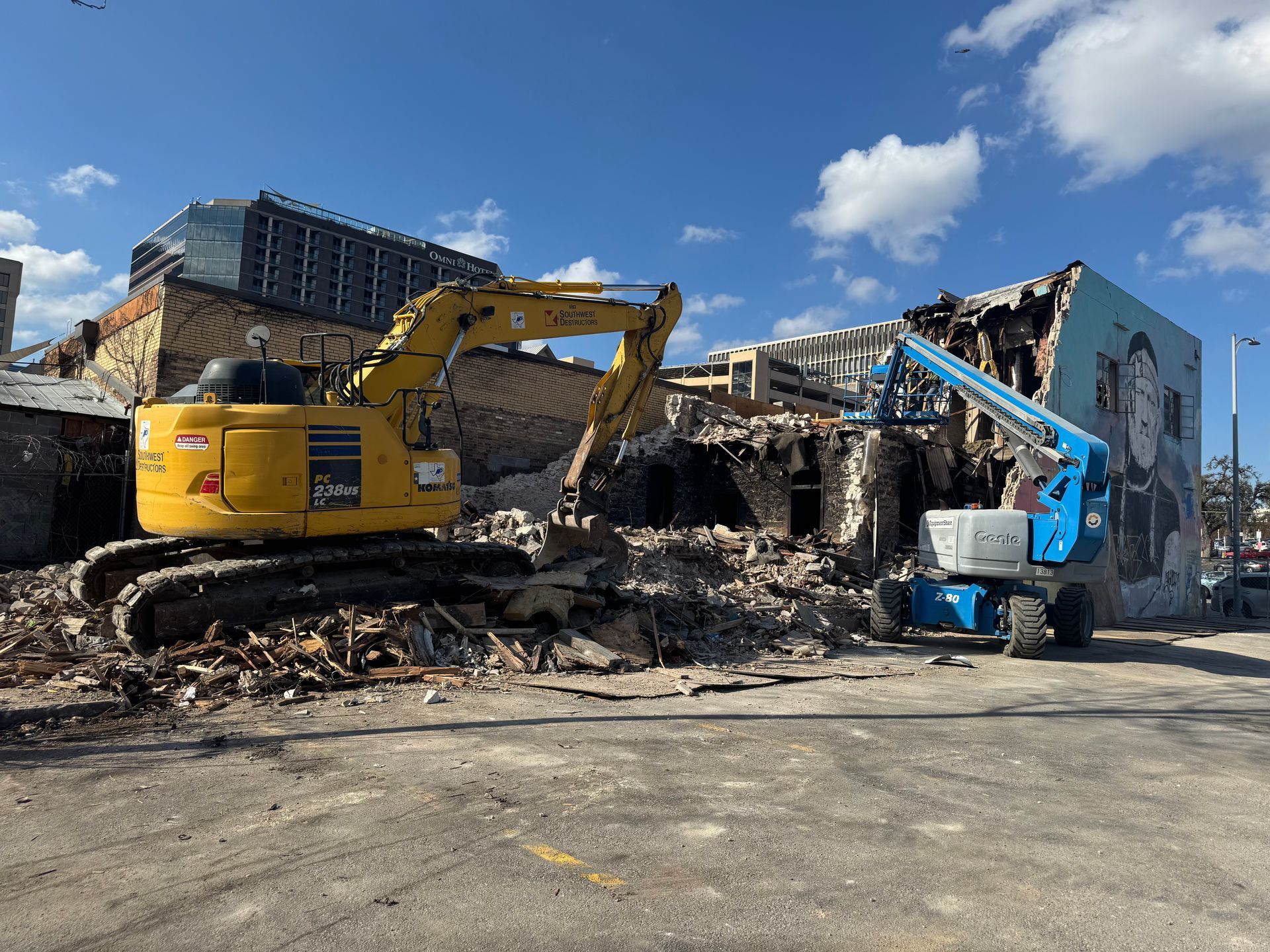 A yellow excavator is demolishing a building in a parking lot.