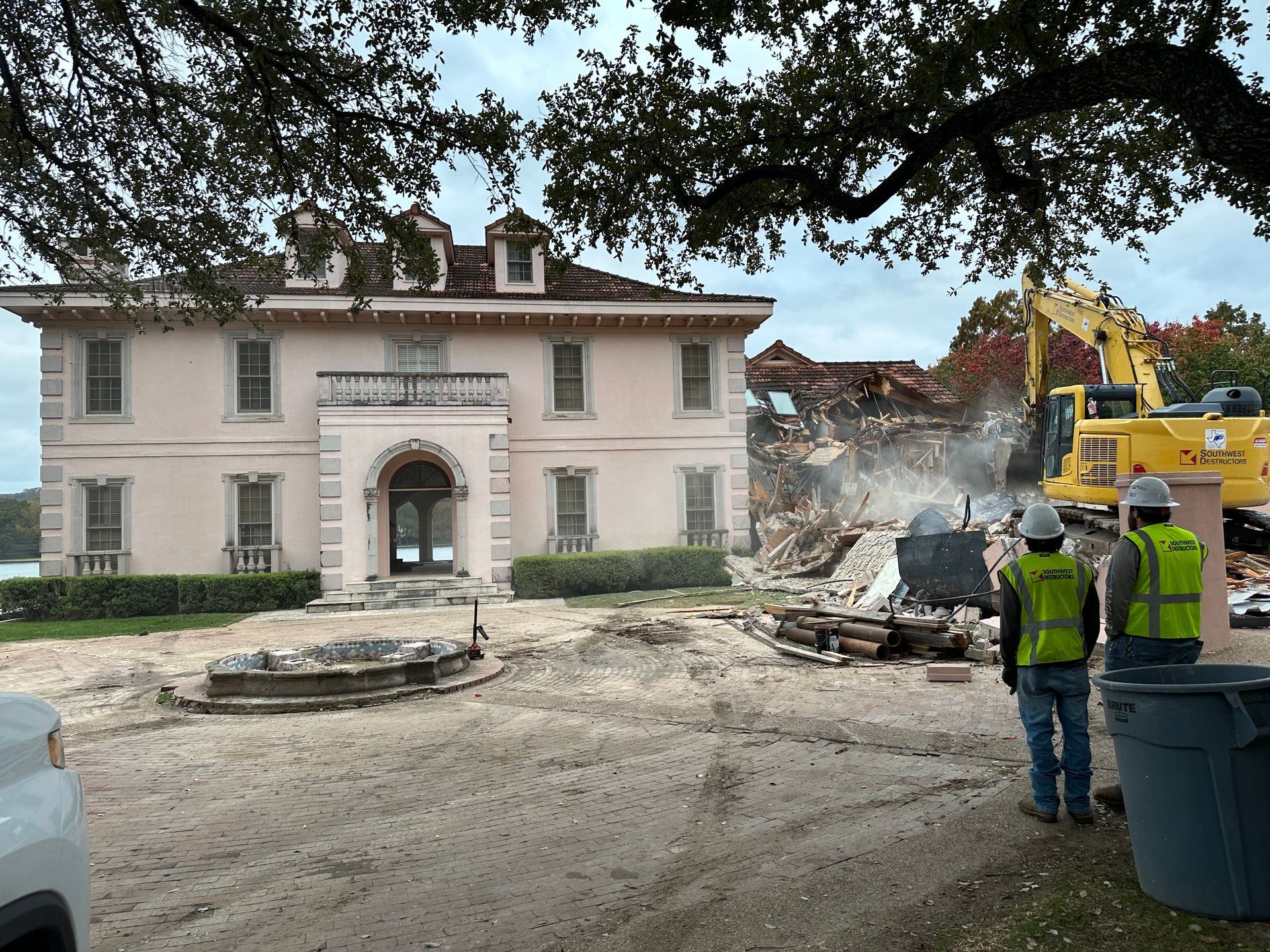 A large pink house is being demolished by construction workers