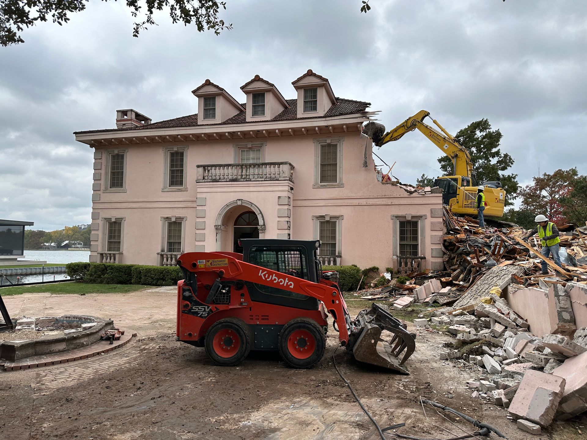 A large pink house is being demolished by a bulldozer.