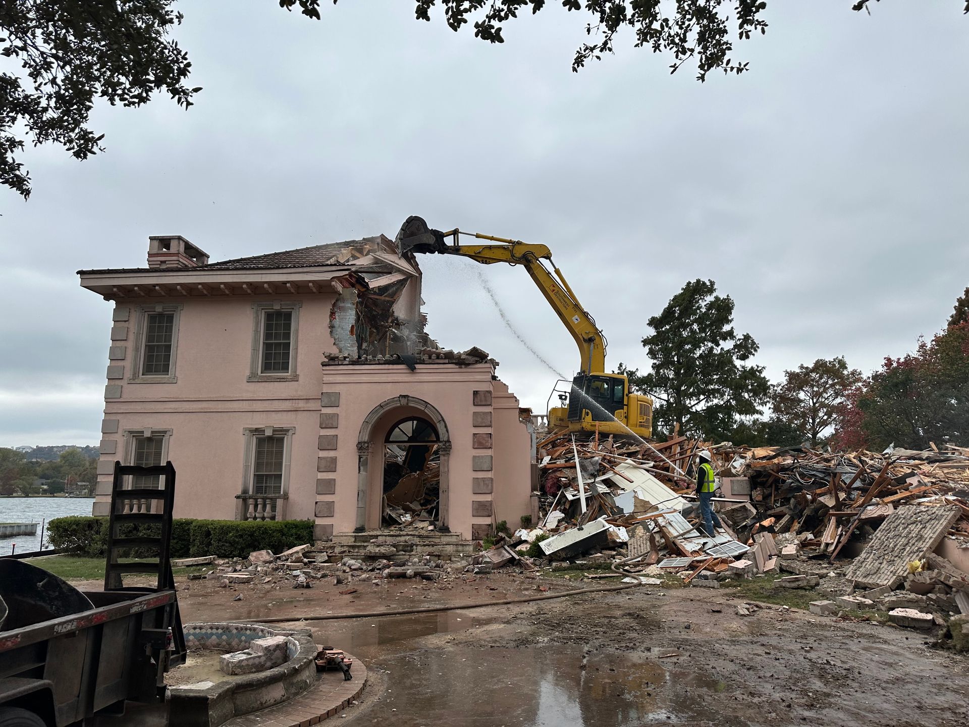A large house is being demolished by a large yellow excavator.