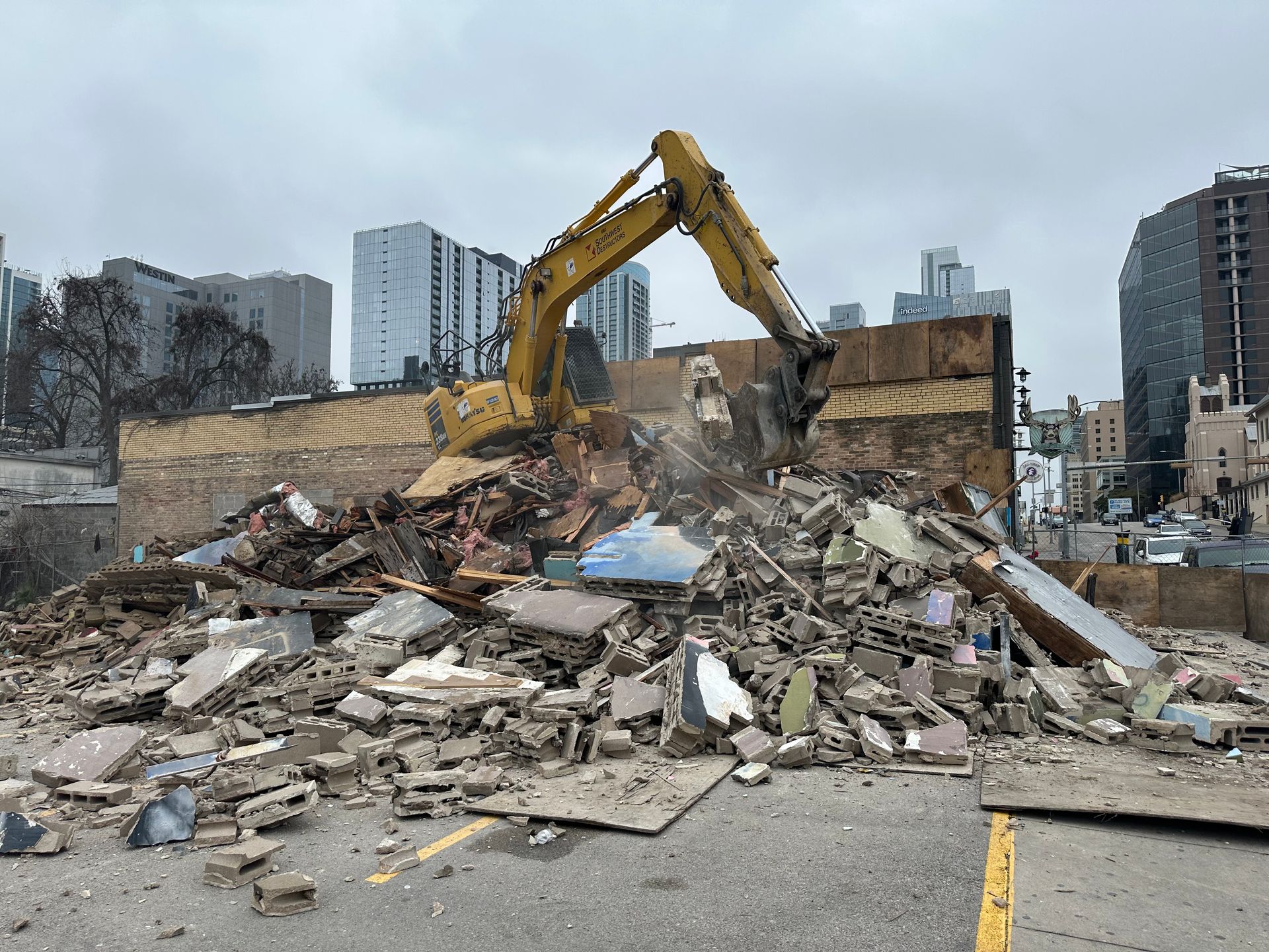 A yellow excavator is demolishing a building in a city.