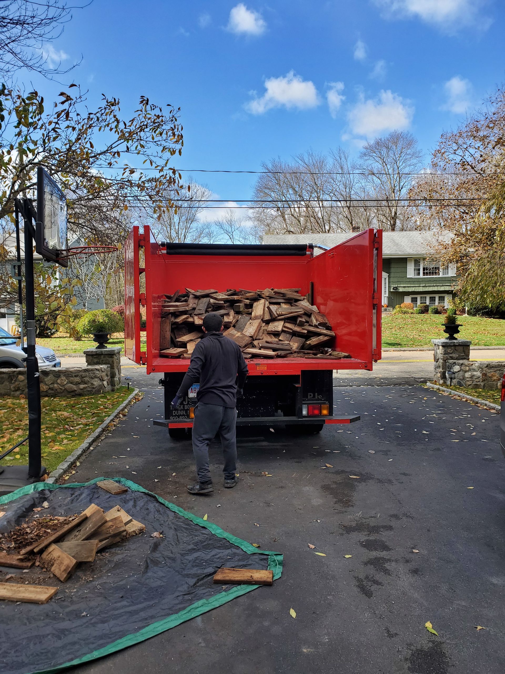 A man is loading wood into a red dump truck.