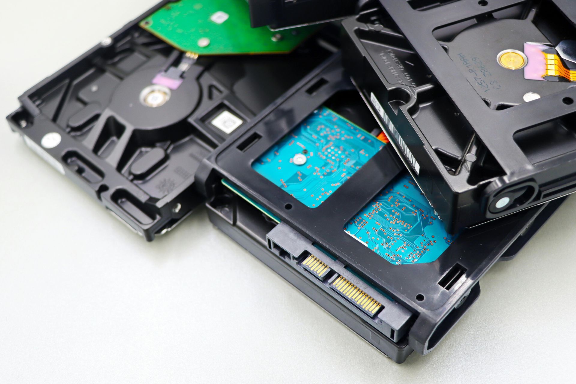 Open hard drives with exposed internal discs and blue circuit boards on a white surface