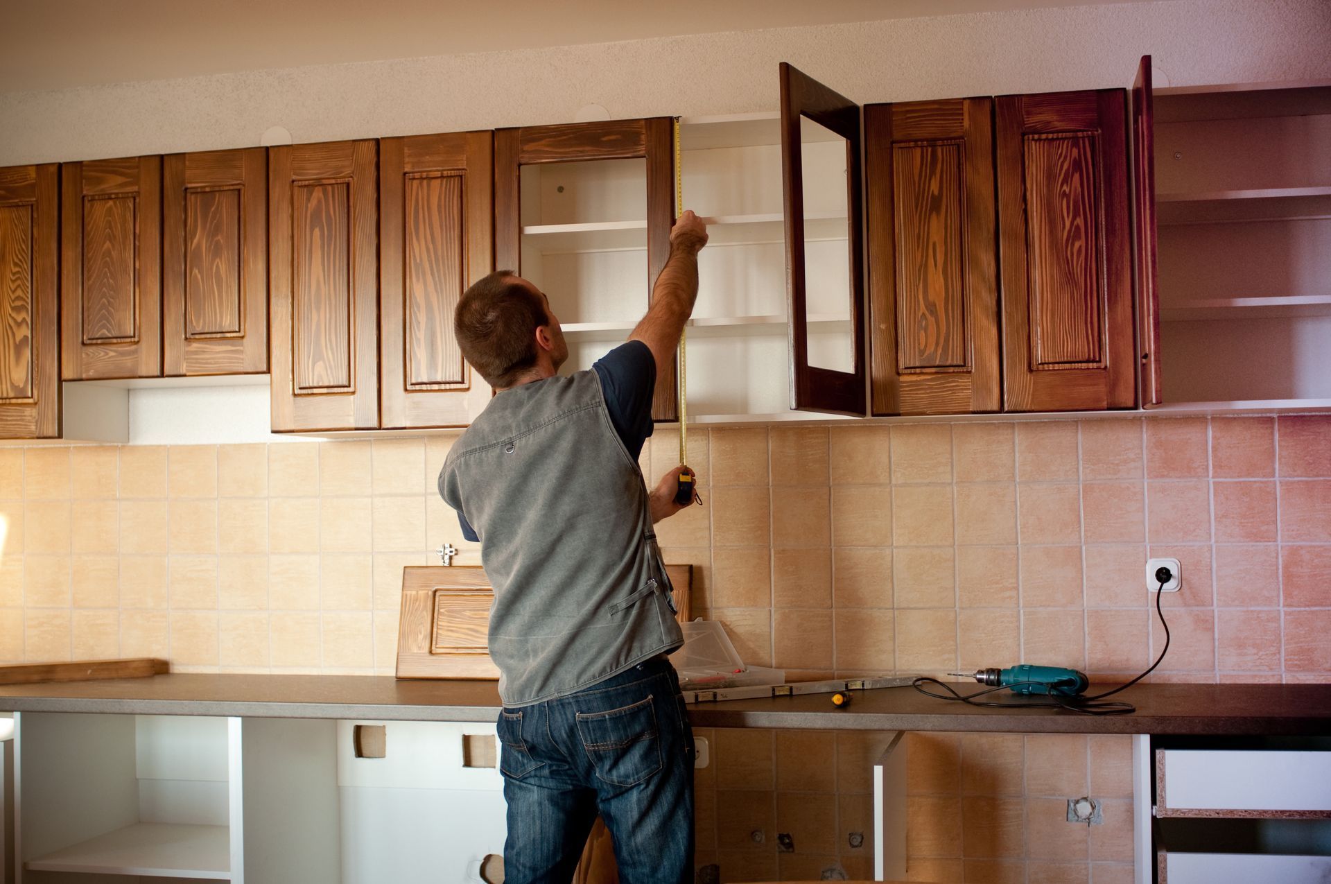 Worker measuring inside a kitchen cabinet during a renovation project.