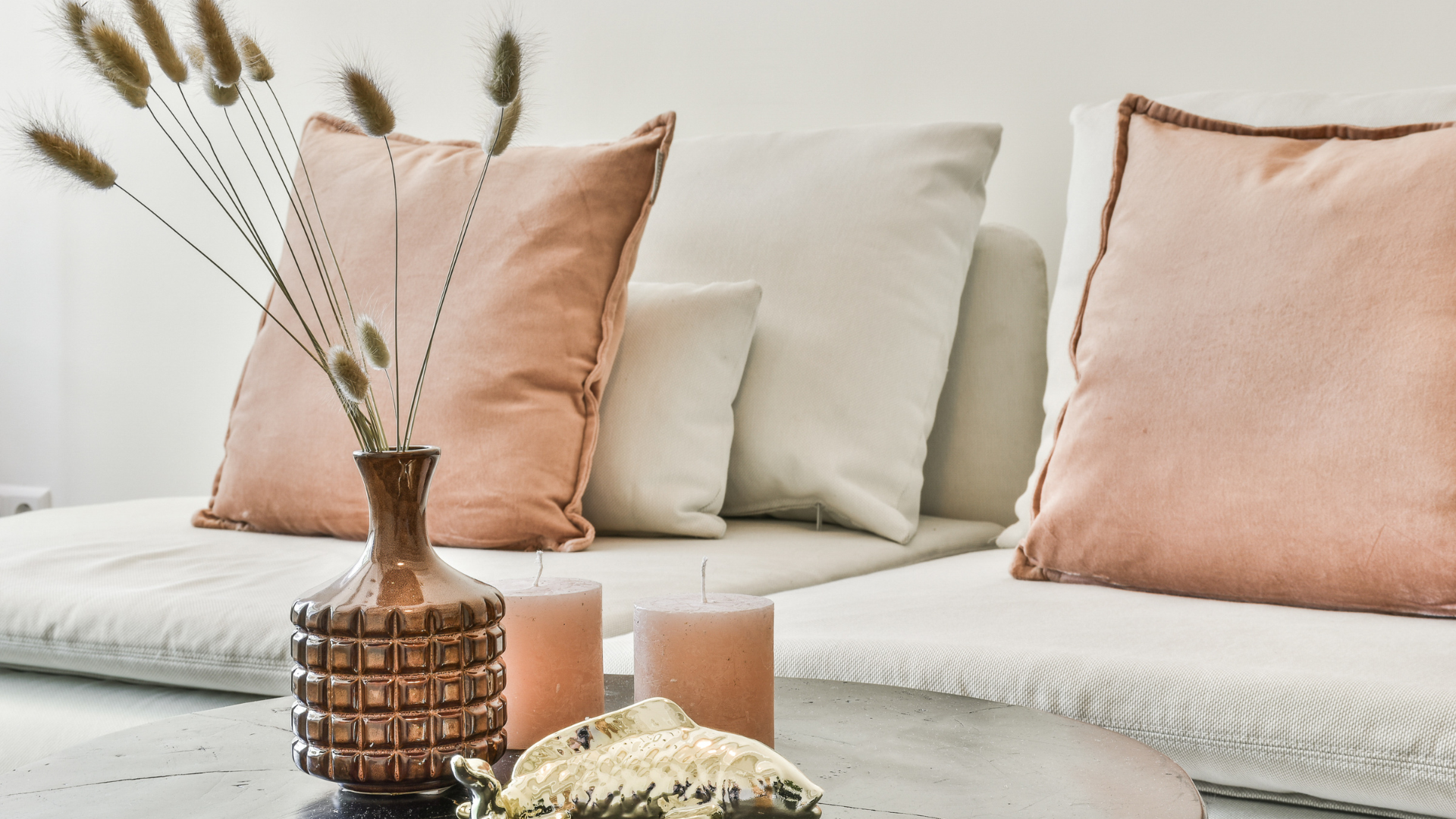 Cream sofa with blush pillows and dried flowers in a copper vase on a white table