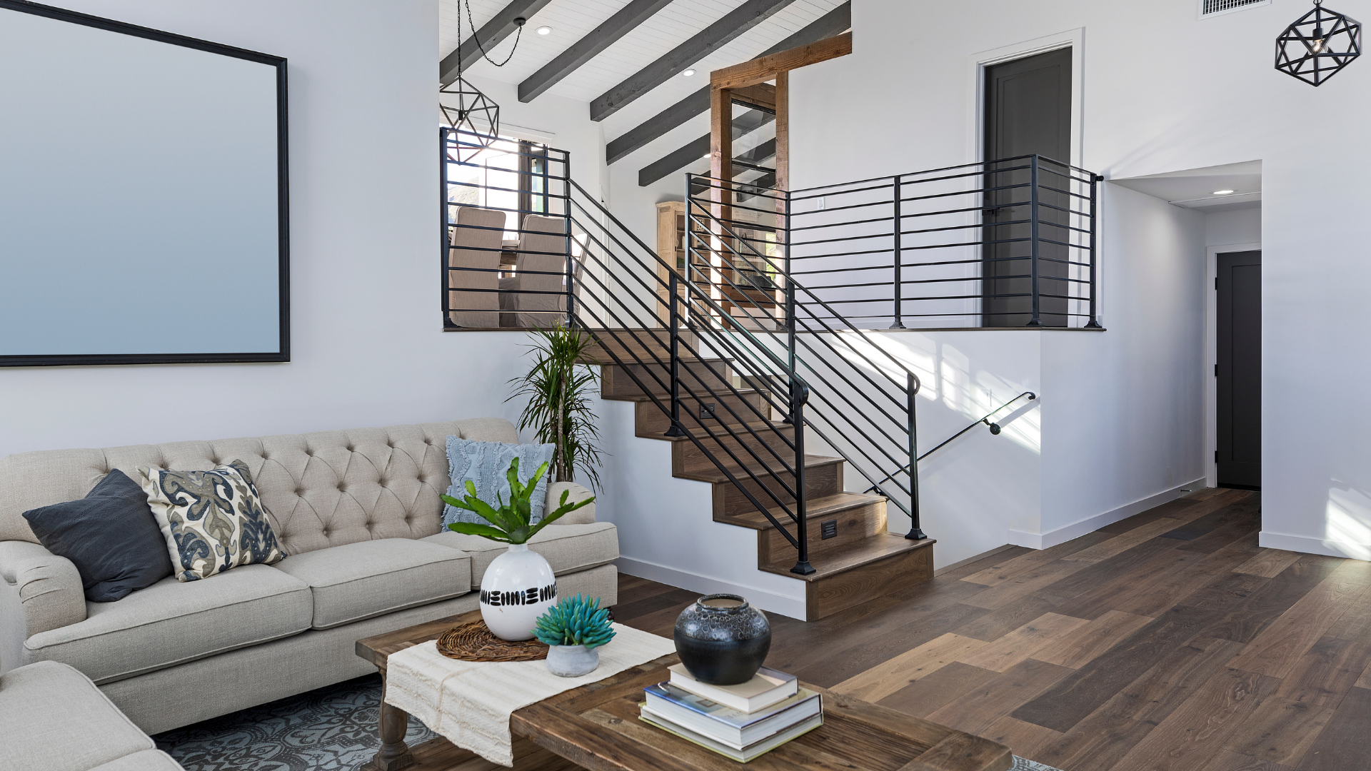 Modern living room with beige sofa, wooden staircase, and white walls with loft railings.