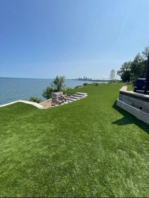 A manicured lawn leading to stone steps overlooking a large body of water with a distant city skyline under a clear sky.