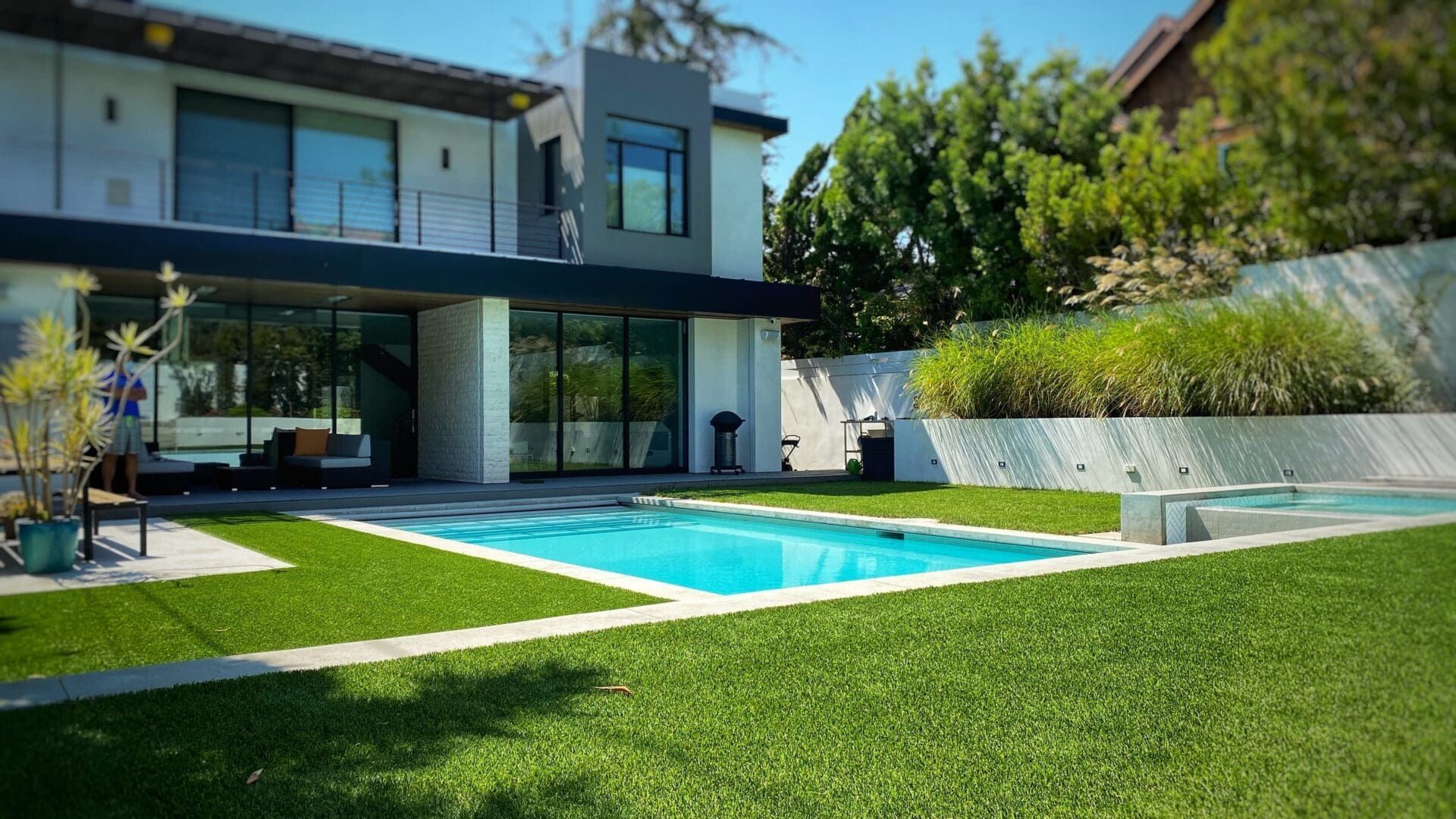 A modern two-story home with a swimming pool and grassy yard on a sunny day.