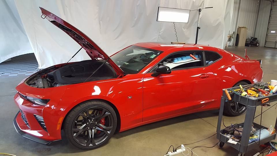 Red sports car with hood open in a garage, next to a tool cart and lights.