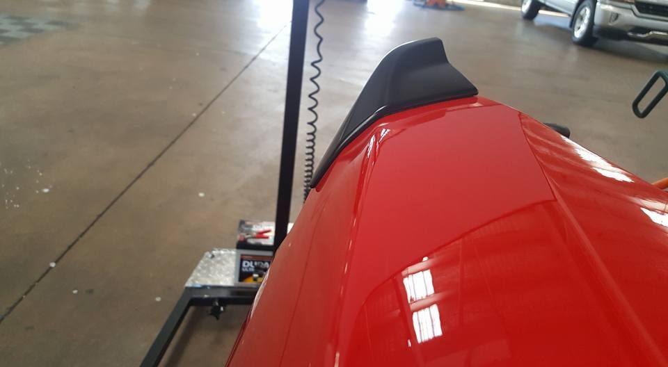 Red vehicle hood in a garage, with a lift post and concrete floor visible.