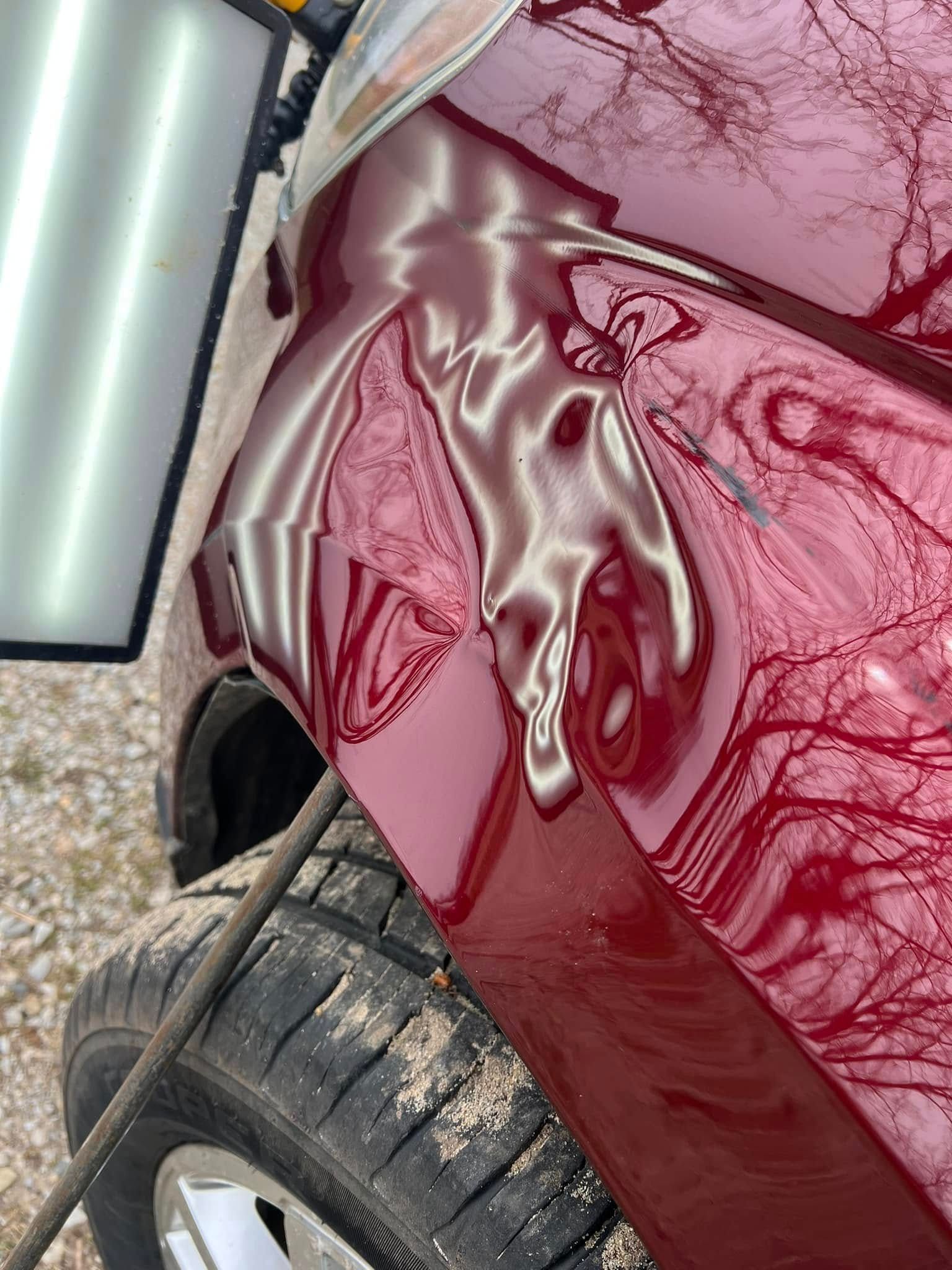 Close-up of a red racing car nose in a garage, with a tow hitch visible on the left.