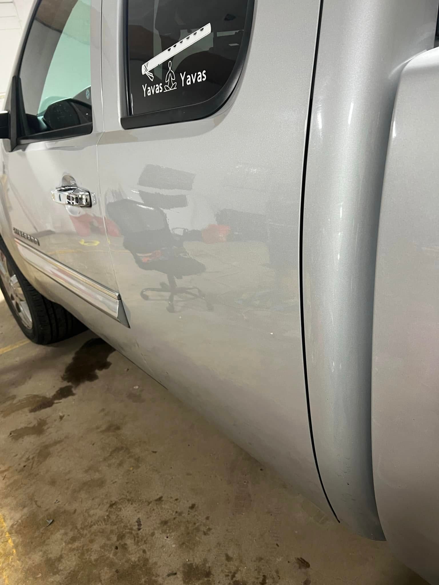 Close-up of white pickup truck side with dented door and muddy floor in a garage