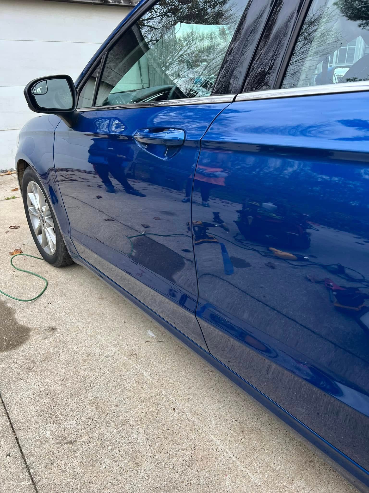 Blue car side panel with noticeable dents and scratches, parked on a driveway.