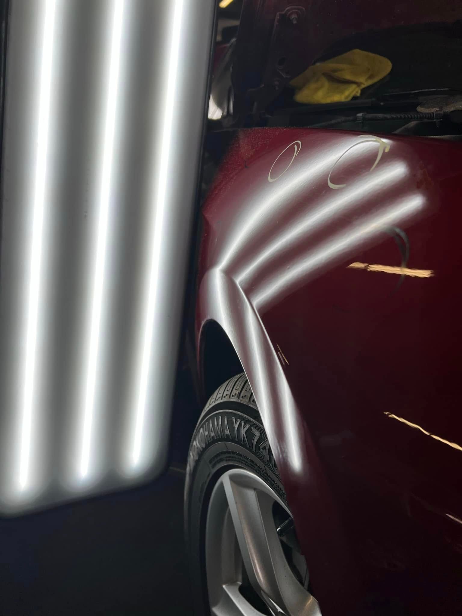 Maroon car fender and wheel beside a reflective metal pole at night