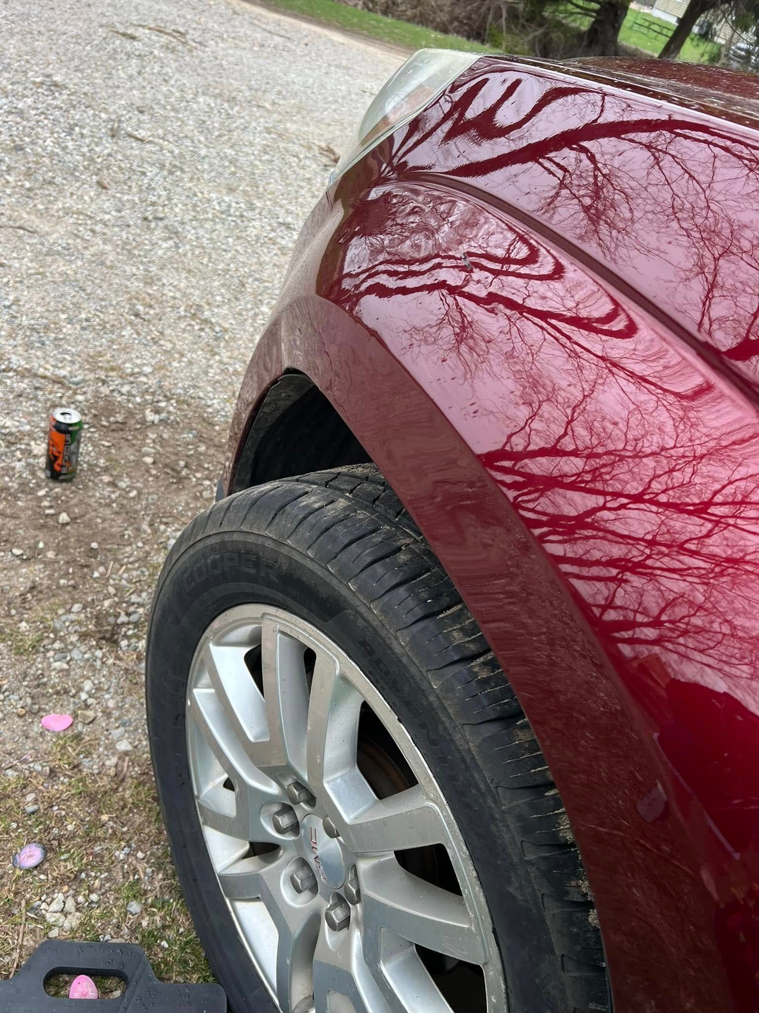 Maroon car front wheel and fender on a gravel driveway, with a small can nearby