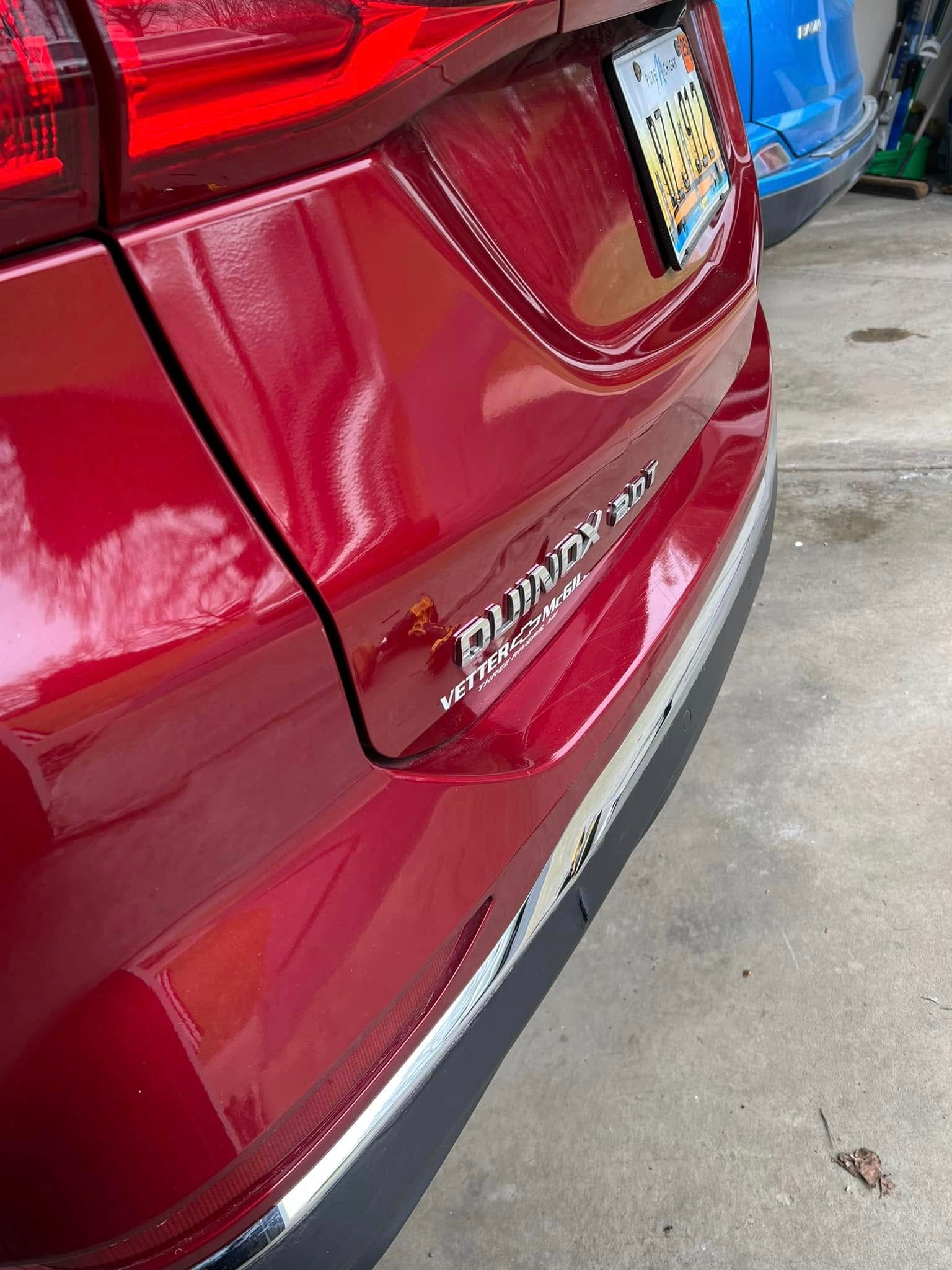 Close-up of a red SUV’s rear hatch and bumper in a parking lot, with a blue car beside it.