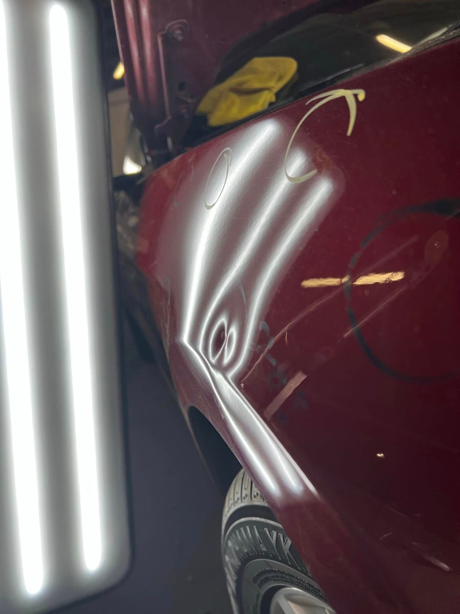 Maroon car fender with a dent, next to a bright vertical light and yellow cloth in a garage