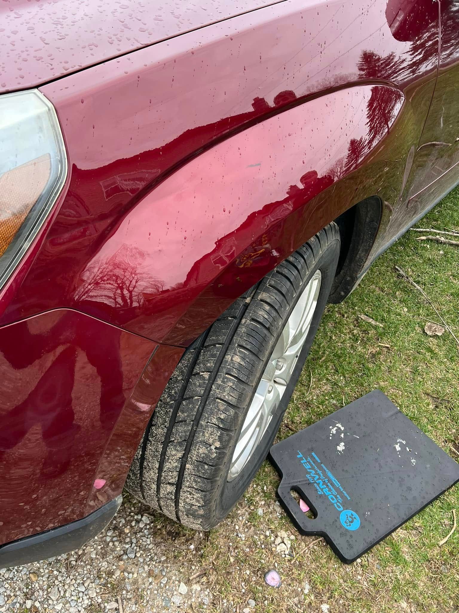 Maroon car with front wheel turned outward, parked on gravel beside a black box near the tire.